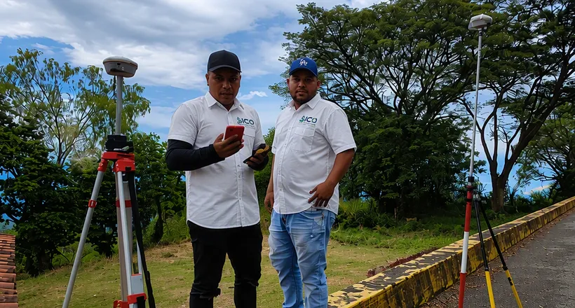 Dos integrantes del equipo de SICO junto a receptores GPS montados en trípodes, al borde de una vía rural